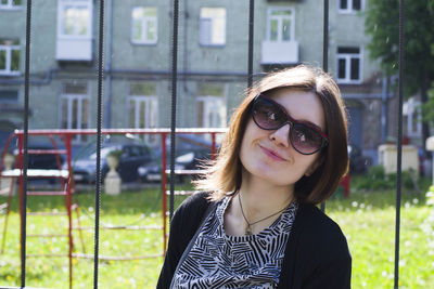 Smiling young woman wearing sunglasses while standing by fence