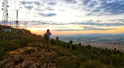 Man standing on landscape against sky during sunset