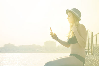 Woman holding cigarette in water against sky