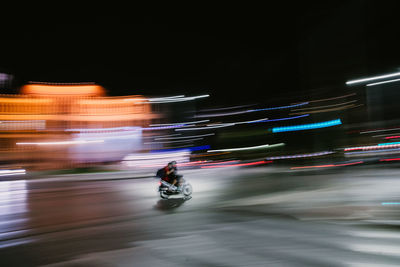 Blurred motion of man riding motorcycle on illuminated road at night
