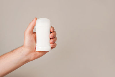 Male hand holding white deodorant on gray background. closeup. copy space