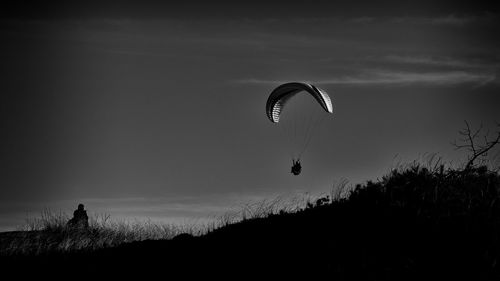 Low angle view of person paragliding against cloudy sky at dusk