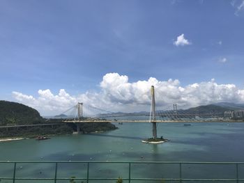 Suspension bridge over sea against cloudy sky