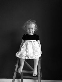 Portrait of cute smiling girl sitting on stool at home