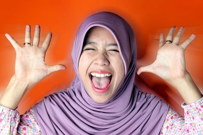 Studio shot of girl in hijab screaming against orange background