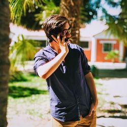 Young man wearing sunglasses talking on smart phone while standing outdoors