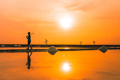 Silhouette people on beach against orange sky