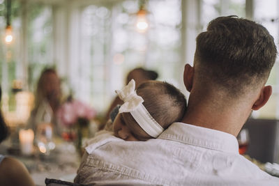 Daughter wearing headband sleeping on father shoulder at dinner party