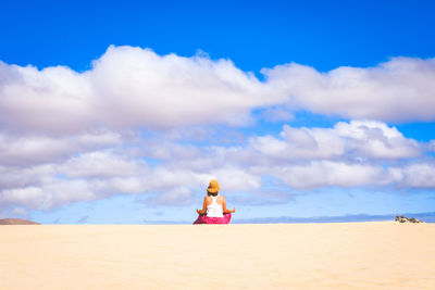 Rear view of woman sitting at sea against sky