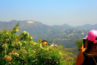 Rear view of woman photographing man with hollywood sign against sky