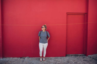 Portrait of young woman standing against red wall