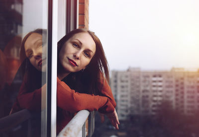 Portrait of woman looking through window against sky