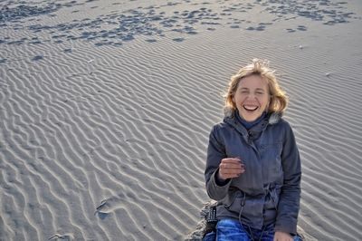 Cheerful young woman sitting on sand at beach