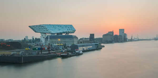 Sea by buildings against sky during sunset