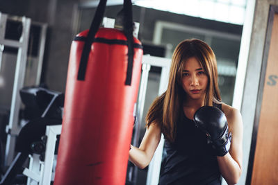 Portrait of young woman practicing boxing with punching bag in gym