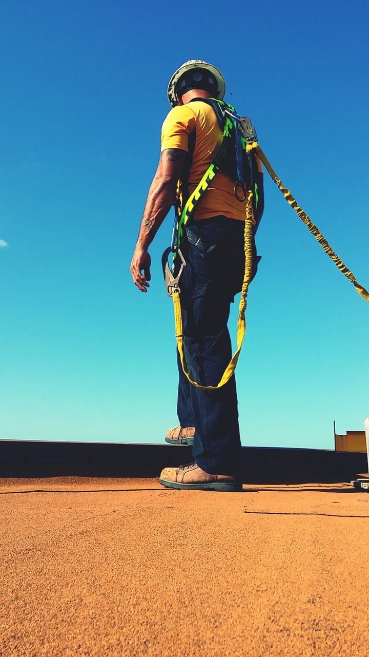 full length, lifestyles, clear sky, leisure activity, casual clothing, blue, rear view, person, sunlight, young adult, standing, childhood, sky, low angle view, arms outstretched, copy space, men, sand