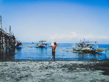 Man carrying bucket while walking against sea