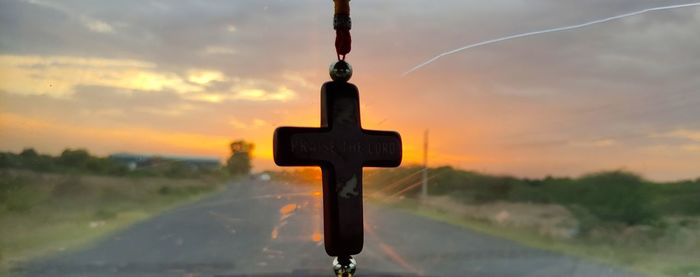 Close-up of cross on land against sky during sunset