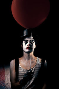 Portrait of young woman with red balloon against black background