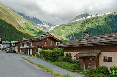 Road by buildings and mountains against sky