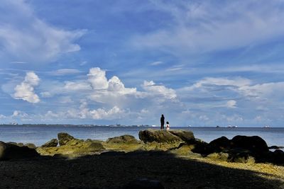 Man standing on rock by sea against sky