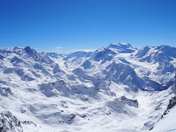 Scenic view of snow covered mountains against blue sky