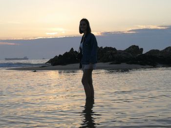 Teenage girl standing in sea against sky during sunset