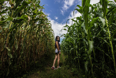 Portrait of woman standing amidst crops on farm against cloudy sky