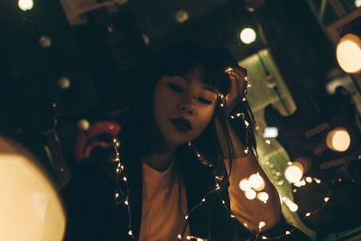 Young woman with illuminated string lights sitting in room