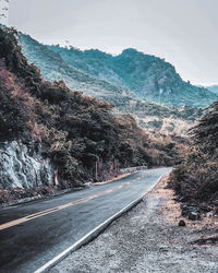 Road amidst trees and mountains against sky