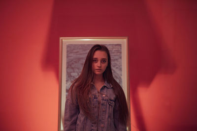 Portrait of woman standing against picture frame and wall