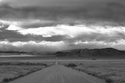 Country road leading towards mountains against cloudy sky
