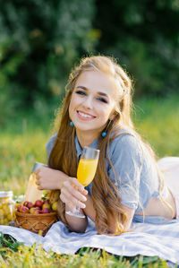 Cute pretty woman with a glass of juice in her hand is lying on a blanket at a summer picnic