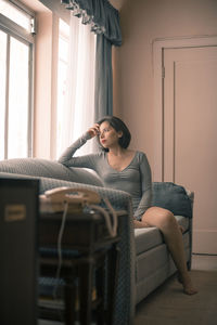 Thoughtful young woman wearing bodysuit on sofa at home