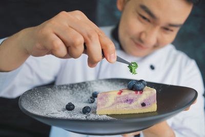 Male pastry chef decorating blueberry cheesecake in the kitchen