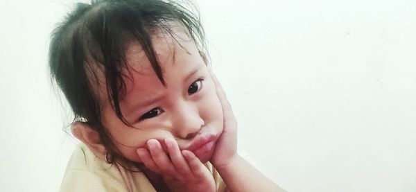 Portrait of cute girl with hands on chin against white background