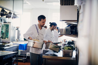 Young male chef carrying containers of food in commercial kitchen