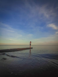 Rear view of woman walking at beach against sky during sunset