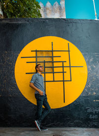Side view of man standing against yellow wall