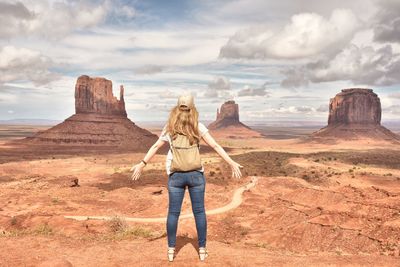Young woman standing on rock formation against sky