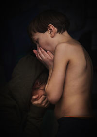 Side view of  shirtless  boy standing near the sitting girl