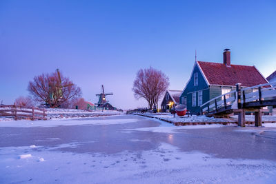 Snow covered houses and trees against clear blue sky