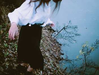 Low section of woman walking on leaves by lake