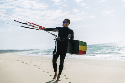 Man with kiteboard standing at beach