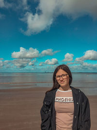 Young woman standing on beach against sky