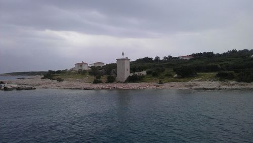 Lighthouse in sea against cloudy sky