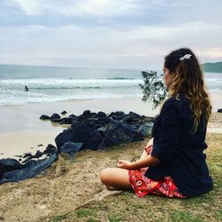 Woman sitting on rock at beach against sky