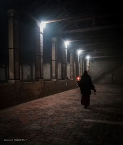 Rear view of man walking on illuminated street at night