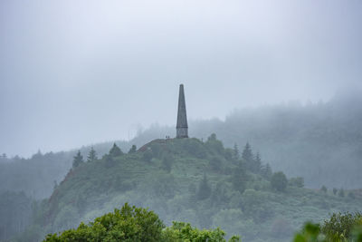 Low angle view of temple on mountain against sky during foggy weather