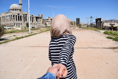 Cropped image of man holding woman hand standing on road